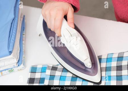 Une femme fer à repasser une chemise d'enfant, gros plan de ses mains. Le concept de soin des vêtements Banque D'Images