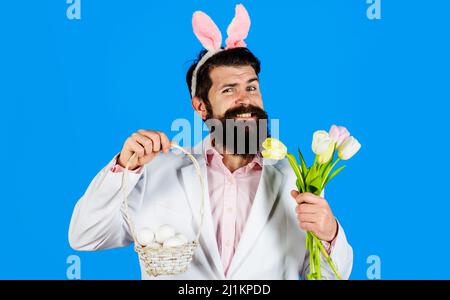 Le jour de Pâques. Chasse aux œufs. Homme barbu souriant avec panier œufs et tulipes. Lapin en vacances. Banque D'Images