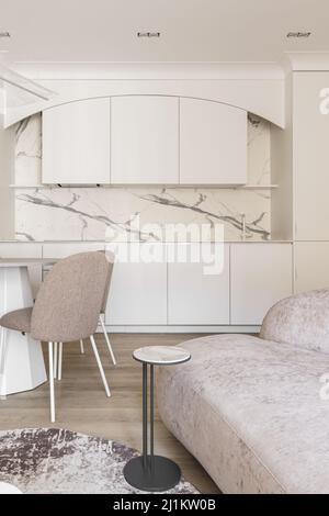 Intérieur moderne de la salle de séjour, tons pastel, table ronde, chaises beige, mobilier de cuisine blanc crème et petite table basse. Min. Tendance Banque D'Images