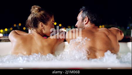 Nous étions de retour dans l'oscillation des choses. Vue arrière d'un couple affectueux et mature qui se détend dans un bain à remous la nuit. Banque D'Images