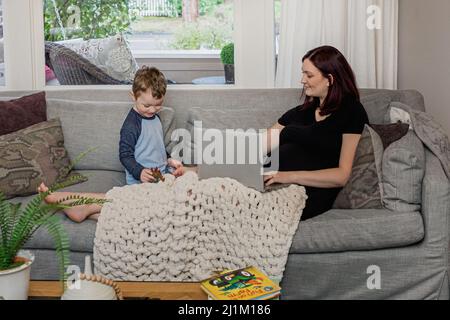 Une belle maman enceinte essayant de travailler à la maison avec un tout-petit Banque D'Images