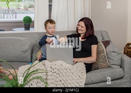 Une belle maman enceinte essayant de travailler à la maison avec un tout-petit Banque D'Images