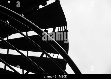 Depuis le dessous, silhouette noire et blanche des marches et rampe d'escalier en spirale contre le ciel gris Banque D'Images