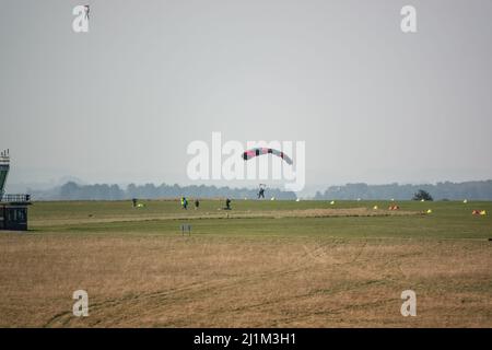 Saut en parachute arrivant sur un terrain d'aviation en herbe, ciel bleu Banque D'Images