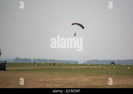 Saut en parachute arrivant sur un terrain d'aviation en herbe, ciel bleu Banque D'Images