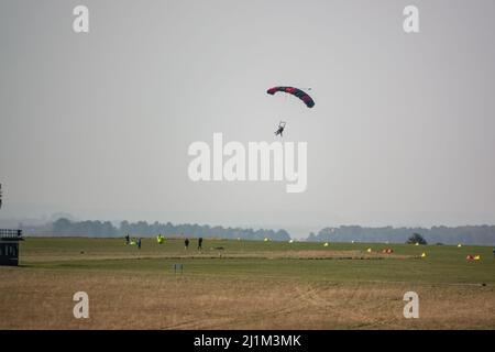 Saut en parachute arrivant sur un terrain d'aviation en herbe, ciel bleu Banque D'Images