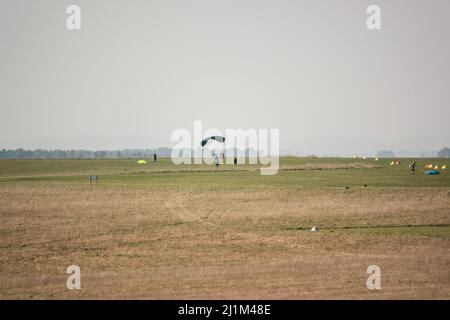 Saut en parachute arrivant sur un terrain d'aviation en herbe, ciel bleu Banque D'Images