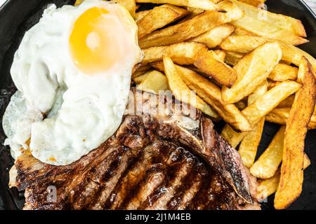 Assiette avec un t-bone grillé ou grillé au barbecue, accompagnée d'une portion de frites et d'un œuf frit. Vue de dessus. Cuisine traditionnelle maison. Clos Banque D'Images