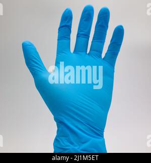 Gants médicaux, de couleur bleue, ne montrant qu'une seule main devant un fond blanc. Banque D'Images