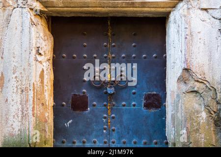 Porte en métal rouillé avec cadenas située à l'extérieur du bâtiment vieillissant et murs en pierre qui s'écroulent en journée Banque D'Images