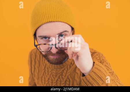 Portrait d'un jeune homme caucasien barbu regardant de manière suspecte tout en abaissant ses lunettes isolé orange fond horizontal . Photo de haute qualité Banque D'Images