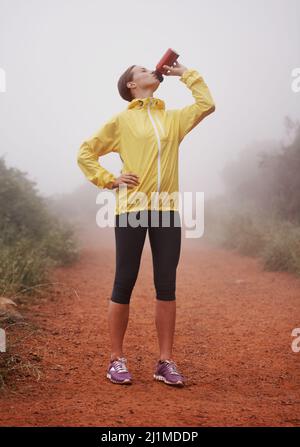 Un verre en chemin. Une jeune femme qui boit de sa bouteille d'eau tout en se tenant sur un sentier forestier. Banque D'Images