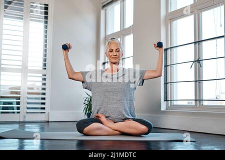 Vous n'avez pas besoin de grands poids pour obtenir une bonne séance d'entraînement. Portrait d'une femme gaie et mûre pratiquant le yoga tout en utilisant des poids à l'intérieur d'un studio Banque D'Images