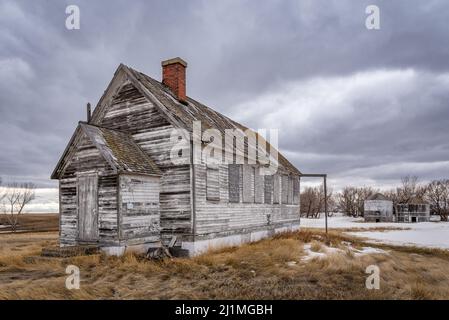 L'extérieur d'une école abandonnée avec des bacs à céréales en arrière-plan dans les Prairies, près de Battrum, en Saskatchewan Banque D'Images