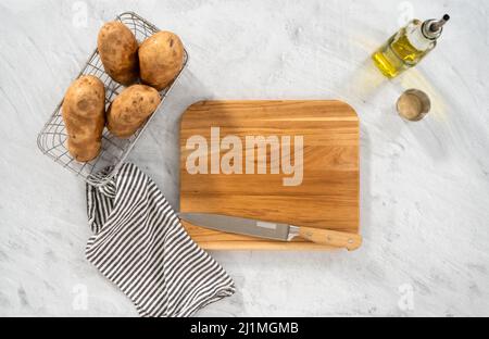 Pose à plat. Couper les pommes de terre en morceaux sur la planche à découper en bois pour les cuire au four. Banque D'Images