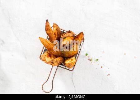 Pose à plat. Quartiers de pommes de terre fraîchement cuits avec épices dans un panier en fil métallique. Banque D'Images