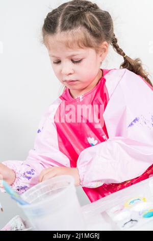 Homeschooling pendant le verrouillage de COVID-19. Petite fille peinture papier mache Pâques lapin figurine avec peinture acrylique. Banque D'Images