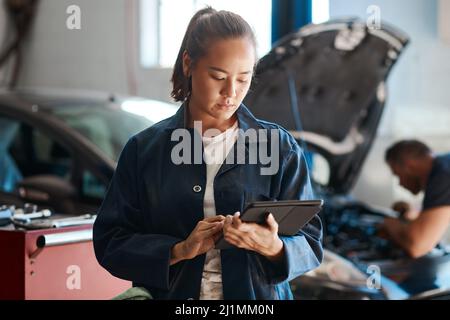 Plus vos connaissances sont diversifiées, plus vous pouvez aider de clients. Photo d'une femme mécanicien utilisant une tablette numérique tout en travaillant dans une réparation automobile Banque D'Images