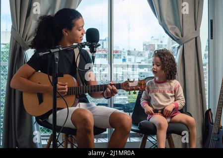 le jeune père vénézuélien latin chante avec la guitare à sa fille assise dans leur studio de musique maison chantant faire de la musique ensemble à la maison, la musique et Banque D'Images