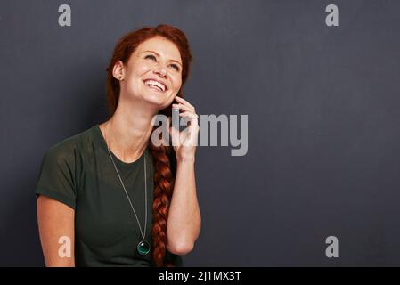 Un seul appel suffit pour passer la journée. Studio photo d'une jeune femme à tête rouge attirante utilisant un téléphone portable. Banque D'Images