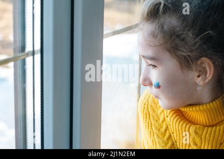 Un enfant triste à la fenêtre avec le drapeau de la Russie, s'inquiète avec des larmes dans ses yeux. Conflit entre la Russie et l'Ukraine, peur Banque D'Images