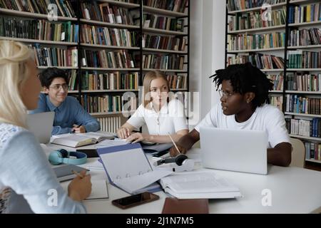 Les étudiants multiraciaux qui étudient ensemble sont assis à table dans la bibliothèque de l'université Banque D'Images