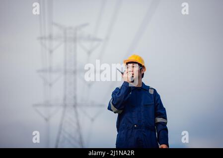 Un ingénieur d'alimentation mâle dans un casque jaune inspecte la ligne d'alimentation sous une ligne électrique haute tension. Banque D'Images