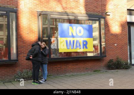 Jeune couple debout à côté d'aucune bannière de guerre contre la guerre en Ukraine dans la vitrine de magasin dans le centre-ville d'Amsterdam, pays-Bas Banque D'Images