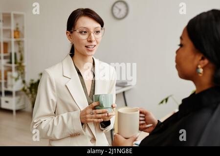 Portrait minimal de deux jeunes femmes qui ont réussi à parler à la pause-café au bureau, concentrez-vous sur une femme d'affaires caucasienne portant des lunettes Banque D'Images
