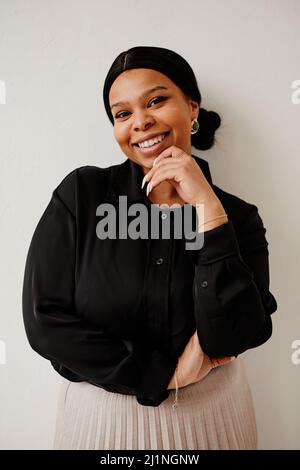 Portrait minimal d'une femme noire élégante souriant avec joie tout en se tenant sur un arrière-plan neutre Banque D'Images