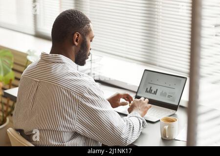 Portrait de l'homme noir adulte avec vue arrière minimale, analysant les données lorsqu'il travaille au bureau à domicile Banque D'Images