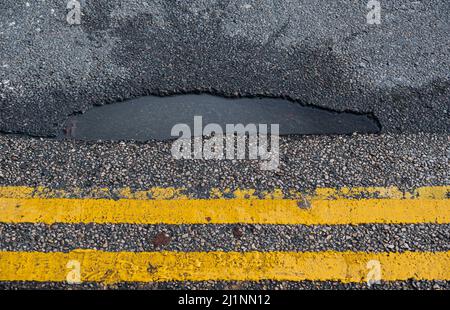 Pothole rempli d'eau de pluie par des lignes jaunes doubles dans un centre-ville britannique Banque D'Images