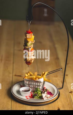 Un gros plan d'un kebab suspendu (viande grillée avec légumes) servi avec des frites Banque D'Images