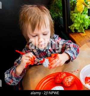 L'enfant se préparant pour Pâques. Peindre les œufs. Œuf de peinture rouge. Banque D'Images