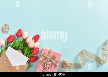 Bannière pour Joyeuses Pâques. Un bouquet de tulipes avec une carte postale et un cadeau et des oeufs de Pâques en bois Banque D'Images