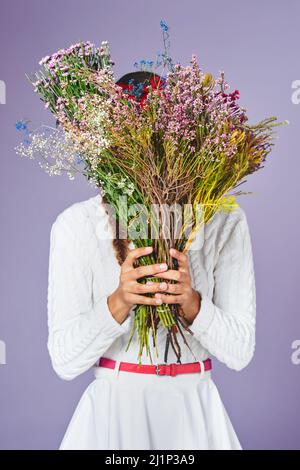 Je préfère cueillir des fleurs au lieu de combats. Photo studio d'une femme debout avec un bouquet de fleurs devant son visage. Banque D'Images