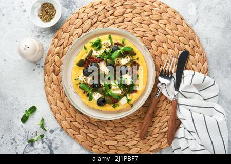 Œufs brouillés. Des œufs brouillés légers, doux et Buttery avec fromage feta, tomates séchées et olives noires sur plaque sur fond de pierre blanche Banque D'Images