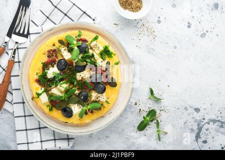 Œufs brouillés. Des œufs brouillés légers, doux et Buttery avec fromage feta, tomates séchées et olives noires sur plaque sur fond de pierre blanche Banque D'Images