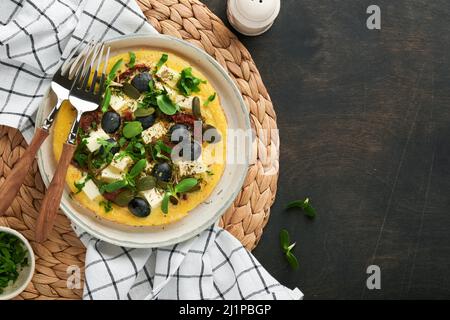 Œufs brouillés. Des œufs brouillés légers, doux et Buttery avec du fromage feta, des tomates séchées et des olives noires sur l'assiette sur le vieux bois sombre rustique Banque D'Images