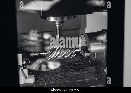 Usine industrielle la fraiseuse CNC traite les pièces à vis sans fin en acier avec des copeaux métalliques. Banque D'Images