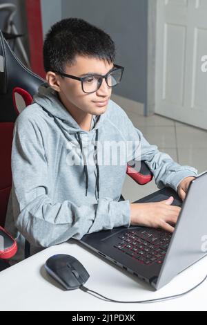 Adolescent garçon à la maison école étudier chambre bureau PC ordinateur lunettes assis regardant les devoirs Banque D'Images