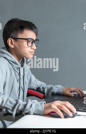 Adolescent garçon à la maison école étudier chambre bureau PC ordinateur lunettes assis regardant les devoirs Banque D'Images