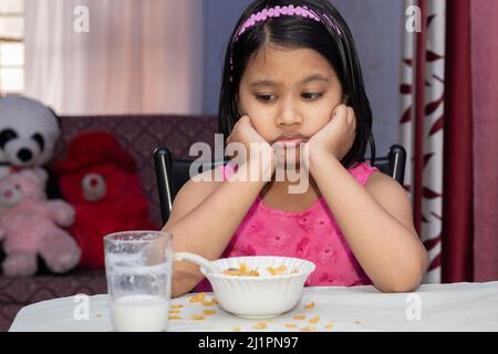 Une petite fille indienne avec un repas incomplet de céréales et de lait qui n'aime pas Banque D'Images