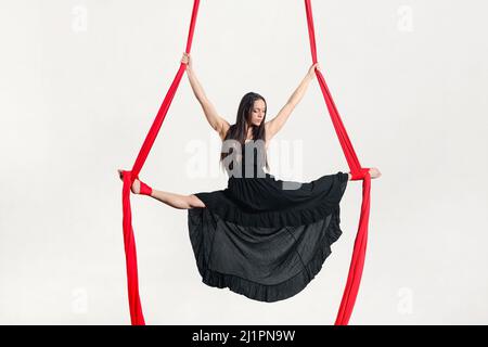 Élégante femme aerialiste en robe exécution fendue sur rubans d'antenne au-dessus du sol sur fond blanc Banque D'Images