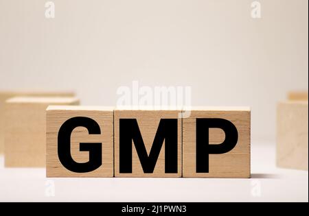 Bonnes pratiques de fabrication. GMP le mot sur des cubes en bois, des cubes se tiennent sur une surface réfléchissante, en arrière-plan est un schéma d'affaires. Entreprise et Banque D'Images