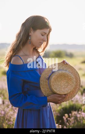 Adorable jeune femme avec chapeau de paille entre les rangées de champs de lavande violette. Fille portant un chapeau à large bord. Banque D'Images