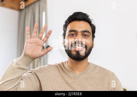 Portrait d'un homme indépendant, souriant et amical, utilisant un ordinateur portable et regardant la caméra. Un gars latin indien dans une chemise élégante et décontractée agitant, tout en travaillant à distance Banque D'Images