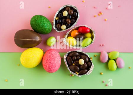 Œufs de Pâques décoratifs colorés et bonbons colorés, chocolats conçus sur une surface rose et vert pastel Banque D'Images