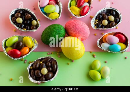 Œufs de Pâques décoratifs colorés et bonbons colorés, chocolats conçus sur une surface rose et vert pastel Banque D'Images