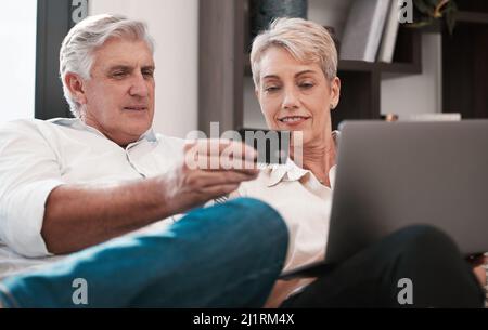 c'est étrange que vous ne connaissiez jamais. Photo d'un couple mature utilisant un ordinateur portable et payant avec une carte de crédit à la maison ensemble. Banque D'Images